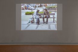 Tematem fotografii jest slajd będący częścią pracy Franciszka Orłowskiego. Slajd wyświetlany jest w wyciemnionej sali. Przedstawia scenę, w której artysta rozmawia z bezdomnym. Obaj mężczyźni siedzą na ławce, zwróceni do siebie twarzami.